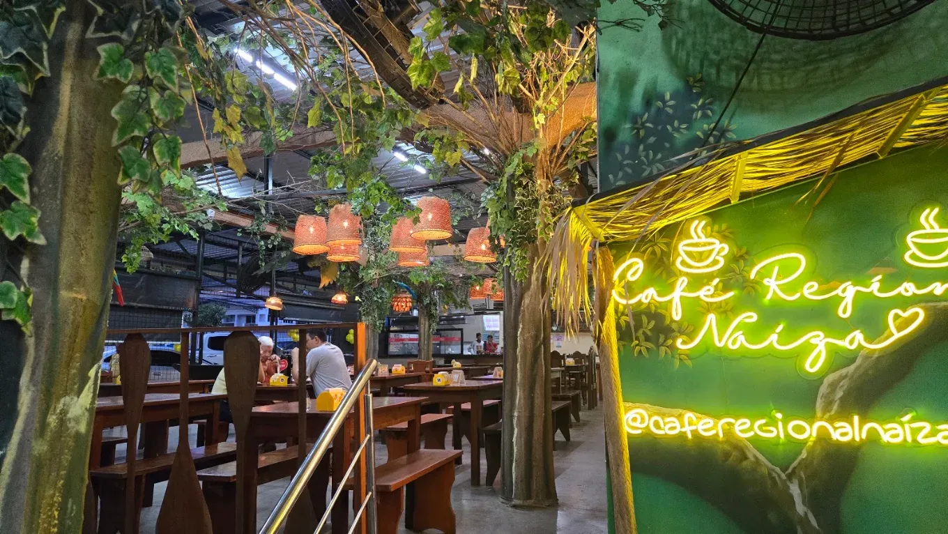 Salão do Naíza com árvores, luminárias de palha e o letreiro em neon do Café Regional Naíza